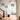 Entryway with soft sky-blue wallpaper, featuring tall whimsical trees, butterflies and birds; patterned wood floor, velvet stool.