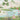 Tranquil pond with vivid flowers, leafy trees, butterflies and dragonfly beneath pastel sky, set against distant mountains.