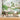 Round dining table and chairs on a neutral rug, backed by a vivid mural wallpaper of trees, flora, birds, pond and misty mountains.