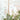 Lush green foliage and white blooms with delicate butterflies and dragonflies set against a serene pale blue sky background.