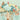 Playful monkeys in a leafy tree, with tiny houses, ladder, swing and a bird below; soft clouds and dotted lines float across a whimsical mural pattern.