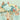 Playful mural wallpaper with a fanciful tree, colorful leaves, tiny houses, two monkeys, a blue bird, and swirling cloud patterns on a soft background.