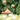 Lush green wallpaper design with domed buildings, cows grazing, monkeys in trees, and dense foliage dotted with pink flowers.