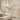 Marble sink in a modern bathroom with gold mirror, wall sconce, and floral wallpaper of birds and butterflies above the counter.