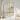 Tall white columns with subtle shadows form a striking mural behind a wicker chair and dried grass vase in a tranquil modern room.