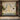 Wallpaper mural with two peacocks on an ornate arch, a red-spotted cow, trees, and a pond with pink flowers, framed by wood panels.