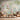 Pair of wooden chairs and a round table with tea set sit before pastel wallpaper with arches, lotus flowers, birds, and foliage.