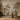 Wicker chair and round table in front of sepia mural wallpaper with classical ruins, trees, and botanical motifs.