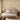 Floral wallpaper in soft hues highlights a serene bedroom with an upholstered bed, green quilt, decorative pillows and gentle natural light.