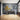 Black-and-white landscape mural spans the wall of a bright, minimalist room with light wood floors, a wooden table, and yellow flowering branches in a tall vase.