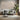 Contemporary living room with a gray sofa, round black table, leafy plant, beige wallpaper, white floral art and soft natural light.