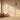 Sunlit room with warm wooden floor, floral-patterned wallpaper, arched window, two vases, and an ornate hanging lamp.